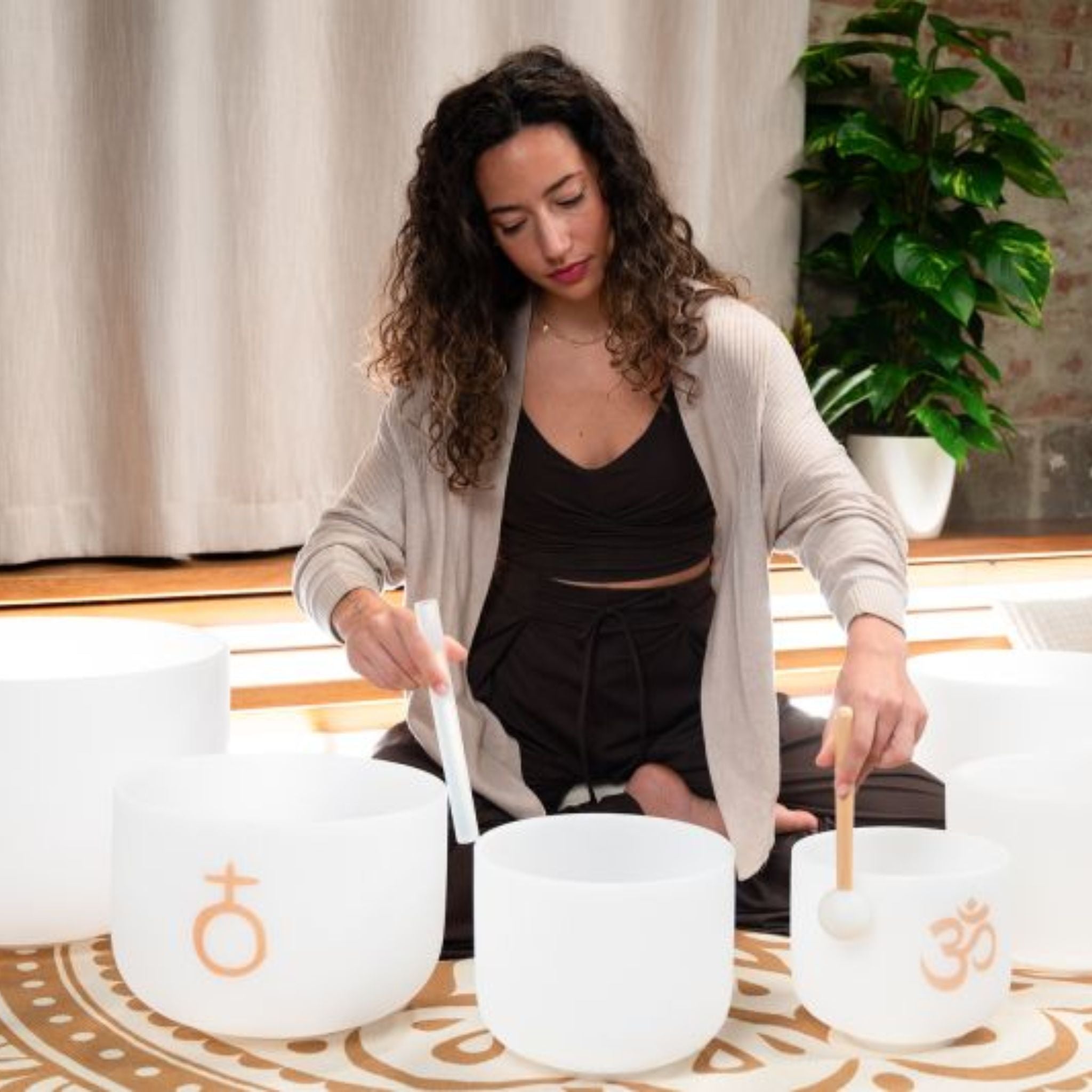 woman playing Meinl Sonic Energy 6-Piece Om Crystal Singing Bowl Set CSBSETOM6 on meditation mat during sound therapy session creating harmonic quartz crystal tones and long-lasting resonance