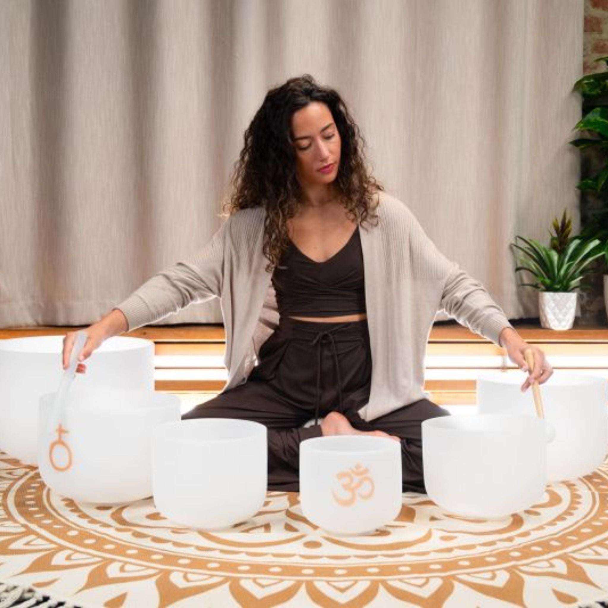 woman using crystal singing bowl mallet with Meinl Sonic Energy 6-Piece Om Crystal Singing Bowl Set CSBSETOM6 in meditation and wellness setting for sound therapy and mindfulness practice