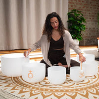 woman playing Meinl Sonic Energy 6-Piece Om Crystal Singing Bowl Set CSBSETOM6 on meditation rug demonstrating immersive crystal bowl soundscapes, Om frequencies, and harmonic resonance for relaxation and sound healing sessions