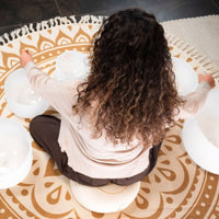rear view of woman seated with Meinl Sonic Energy 6-Piece Om Crystal Singing Bowl Set CSBSETOM6 arranged on meditation mat during sound therapy, mindfulness, and immersive crystal bowl practice session