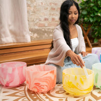 woman playing Meinl Sonic Energy 7-Piece Marble Crystal Singing Bowl Chakra Set 432Hz MCSBSETCHA from front view demonstrating immersive crystal bowl tones and harmonic resonance for meditation and sound exploration