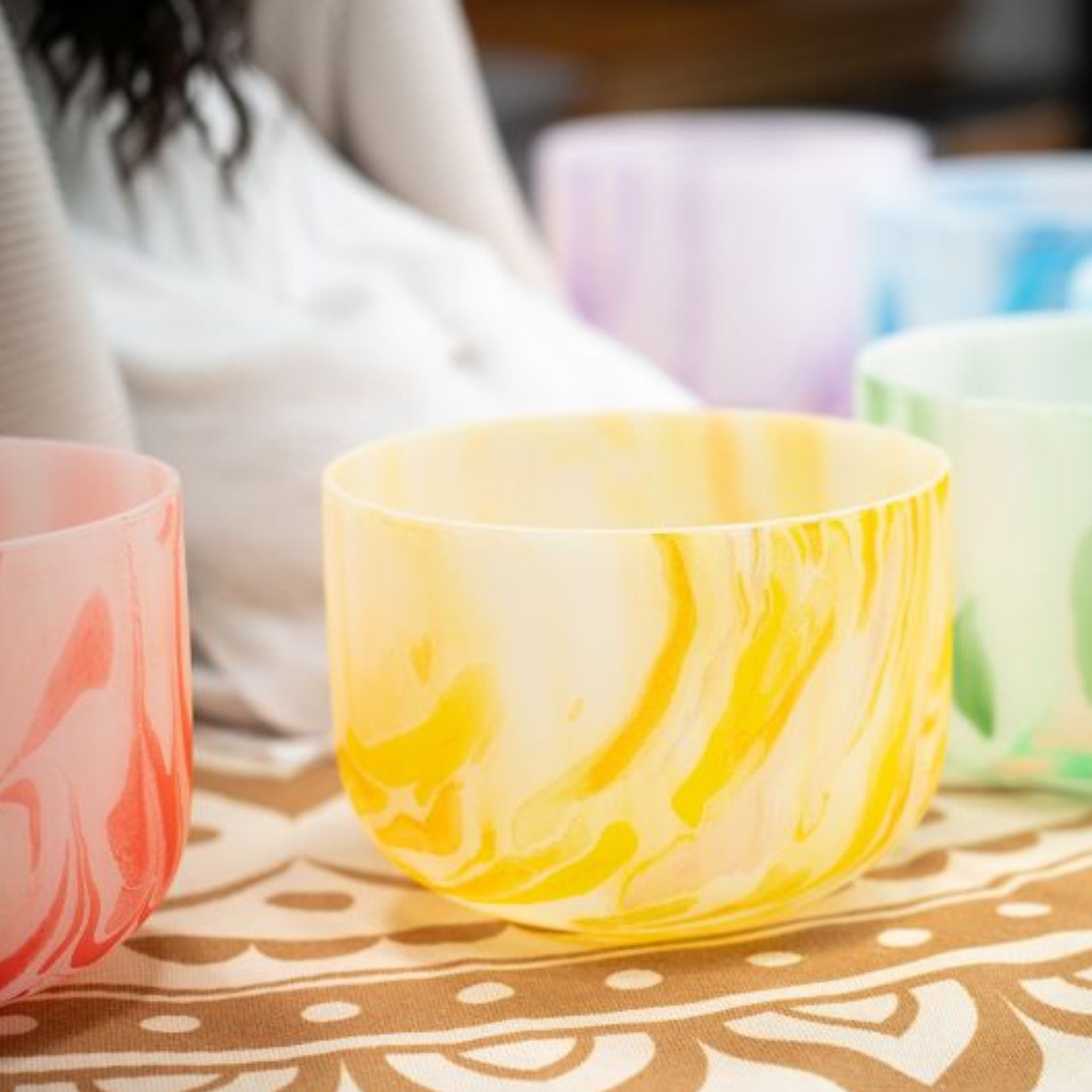 woman playing Meinl Sonic Energy 7-Piece Marble Crystal Singing Bowl Chakra Set 432Hz MCSBSETCHA on floor mat showing chakra-coloured quartz crystal singing bowls used for meditation, sound therapy, and immersive sound exploration