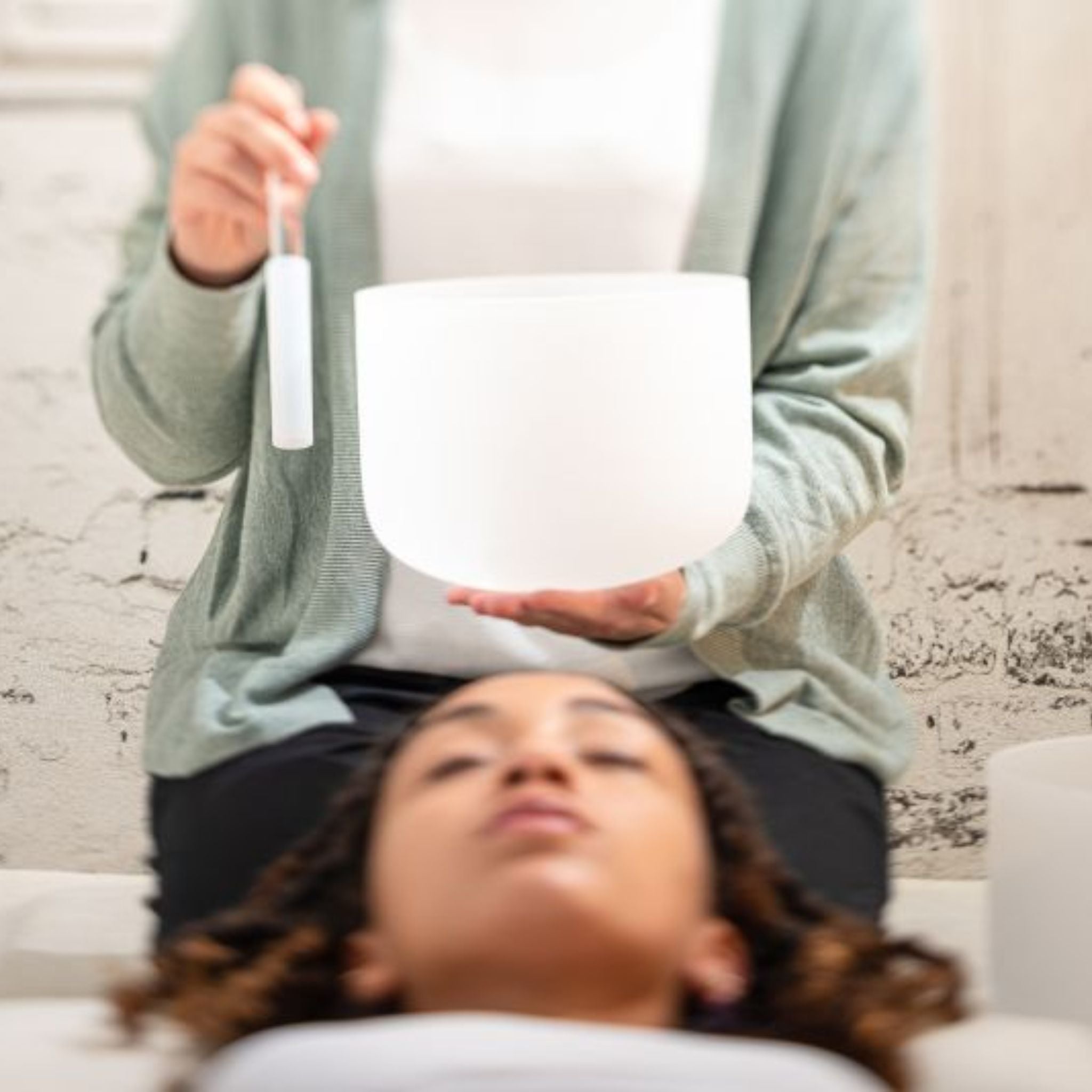 woman holding a Meinl Sonic Energy 8 inch White Frosted Crystal Singing Bowl B4 432Hz Crown Chakra CSB8B above another woman during a sound healing session, creating resonant quartz crystal tones for relaxation, meditation, and wellness practices.