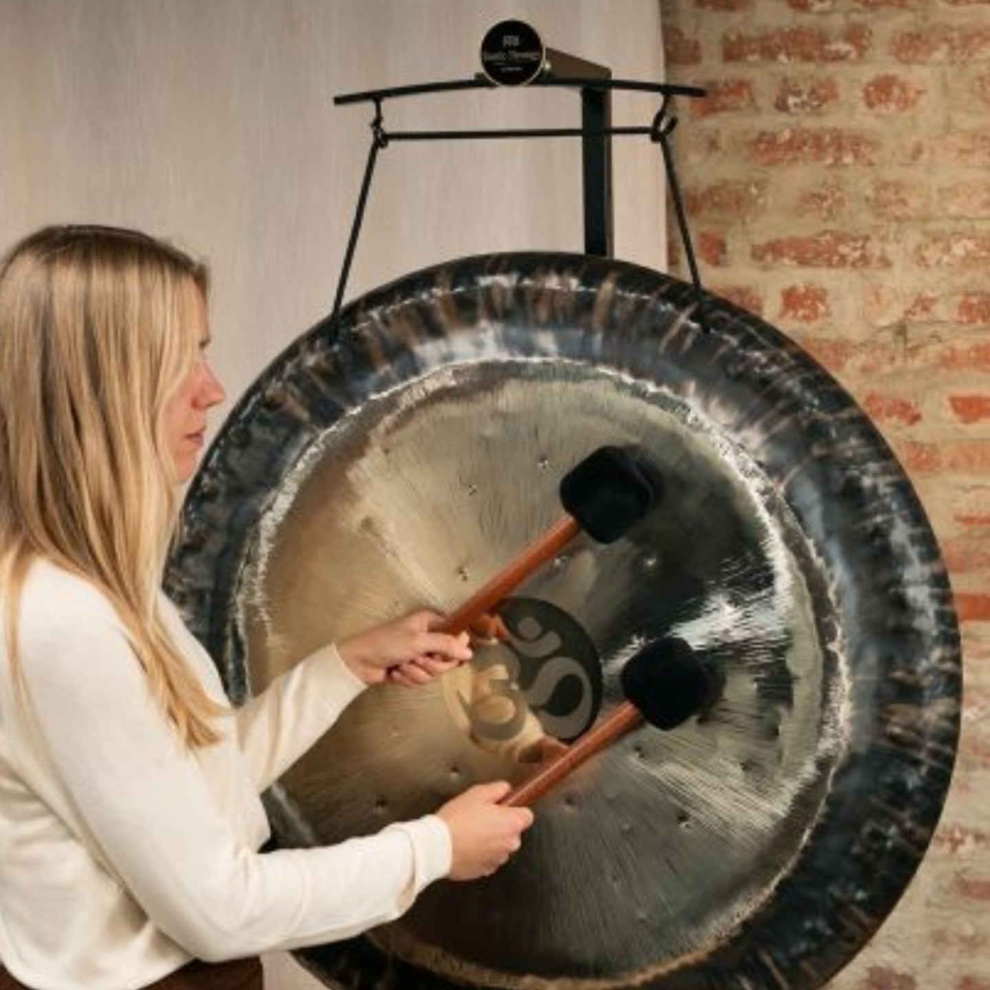 woman playing gong suspended from gong stand with nylon gong cord during sound healing and meditation session