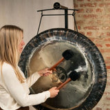 woman playing gong suspended from gong stand with nylon gong cord during sound healing and meditation session