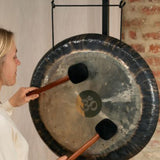 woman playing gong suspended from gong stand with nylon gong cord during sound healing and meditation session