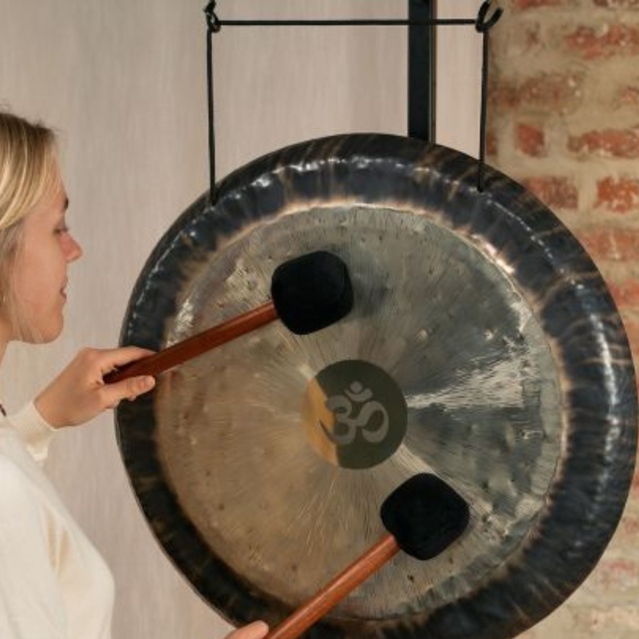 woman playing gong suspended from gong stand with nylon gong cord during sound healing and meditation session
