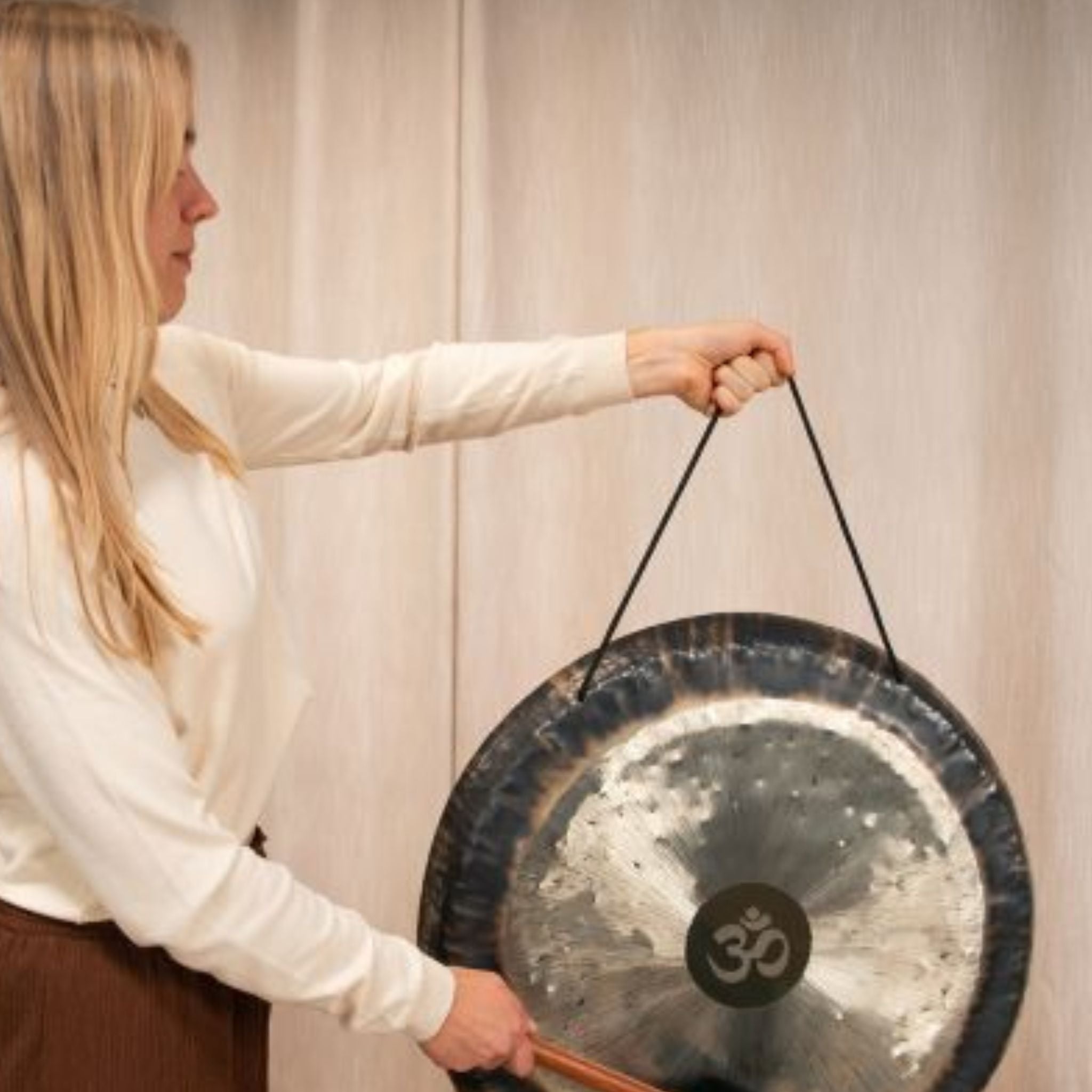 woman holding gong suspended with nylon gong cord while playing with mallet during sound healing session