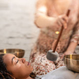 Sound therapist using the Meinl Sonic Energy Medium Felt Tip Mallet – Singing Bowl SB-PM-MF-M to play a metal singing bowl during a sound therapy session with a person lying down.