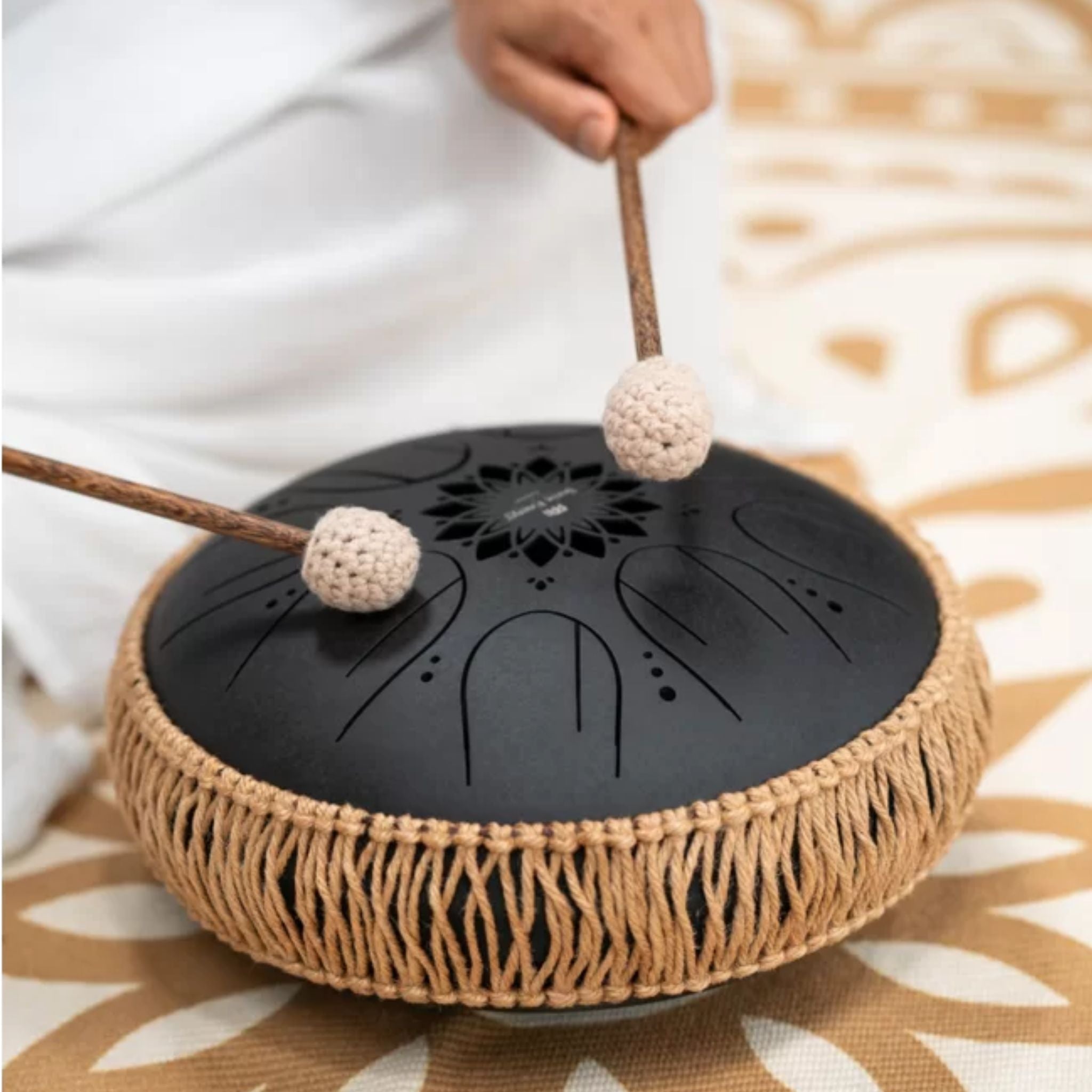Woman playing the Meinl Sonic Energy Medium Octave Steel Tongue Drum 10" B Minor 432 Hz MOSTD1BK while seated on a Meinl Sonic Energy meditation rug.