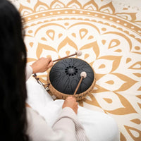 Over-the-shoulder view of a woman playing the Meinl Sonic Energy Medium Octave Steel Tongue Drum 10" B Minor 432 Hz MOSTD1BK with the included soft mallets.
