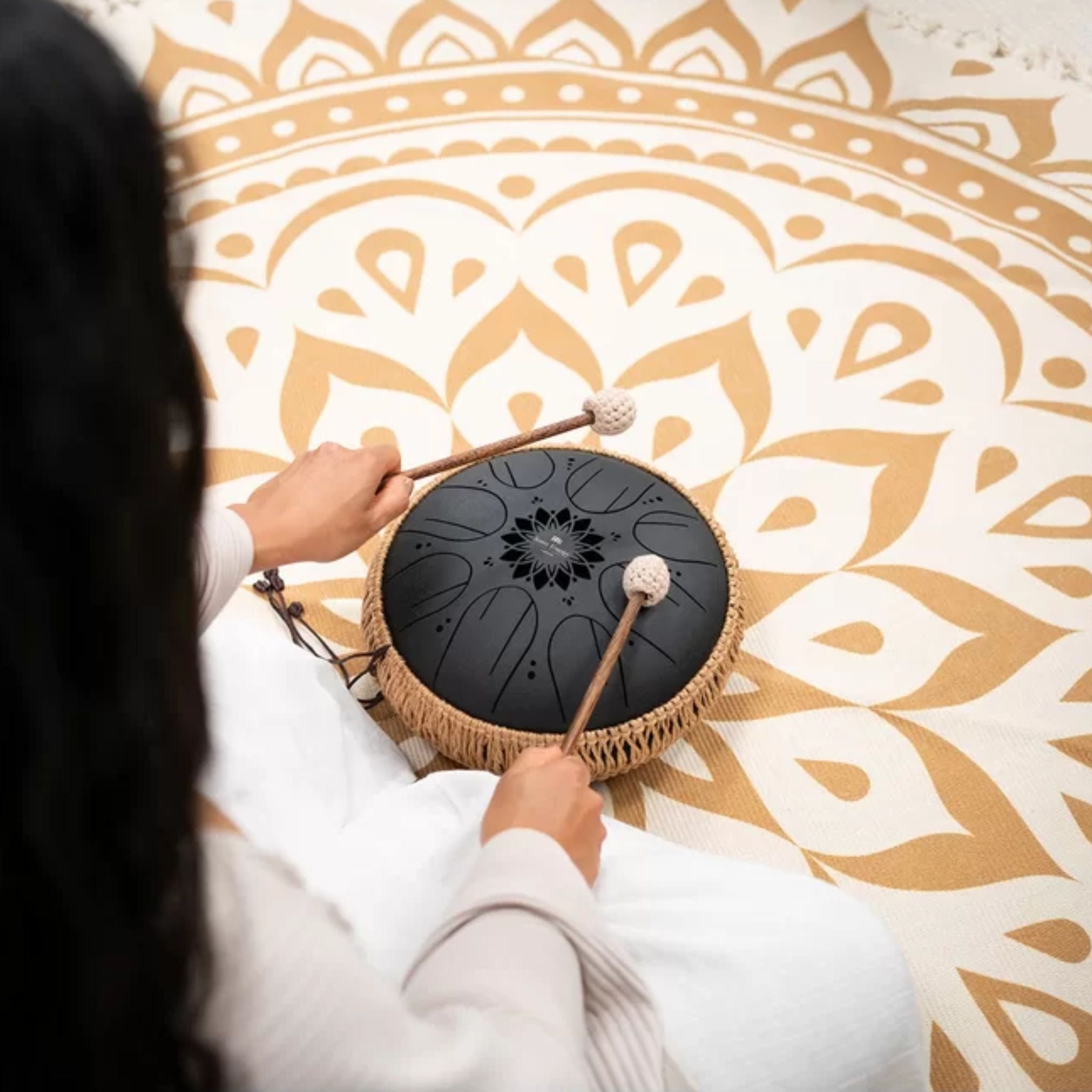 Over-the-shoulder view of a woman playing the Meinl Sonic Energy Medium Octave Steel Tongue Drum 10" B Minor 432 Hz MOSTD1BK with the included soft mallets.