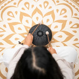 Overhead view of a woman playing the Meinl Sonic Energy Medium Octave Steel Tongue Drum 10" B Minor 432 Hz MOSTD1BK with the included soft mallets.