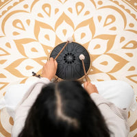 Overhead view of a woman playing the Meinl Sonic Energy Medium Octave Steel Tongue Drum 10" B Minor 432 Hz MOSTD1BK with the included soft mallets.
