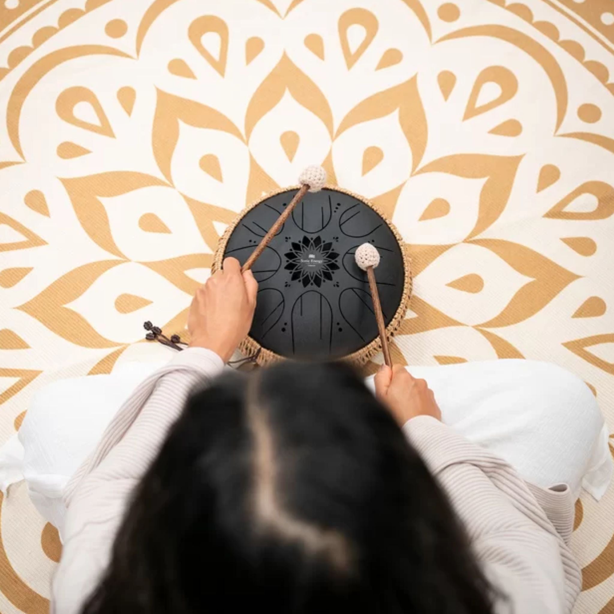 Overhead view of a woman playing the Meinl Sonic Energy Medium Octave Steel Tongue Drum 10" B Minor 432 Hz MOSTD1BK with the included soft mallets.