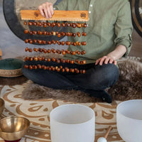 Person seated cross-legged on a meditation rug holding the Meinl Sonic Energy Pala Chimes SPCH by the mahogany bar.