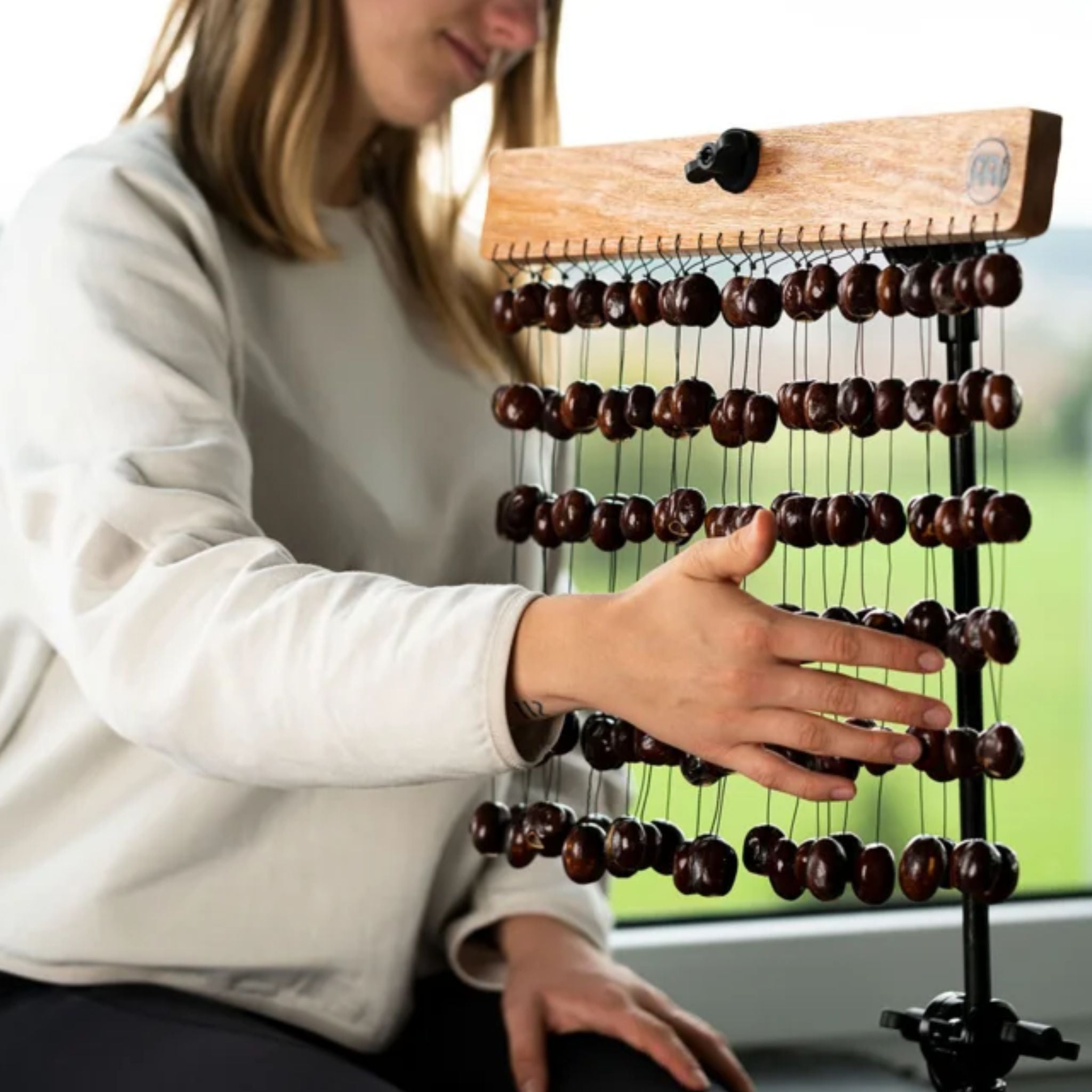 Young woman playing the Meinl Sonic Energy Pala Chimes SPCH while holding the mahogany bar with one hand.