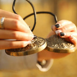 Close-up of a woman’s hands holding Meinl Sonic Energy TINGSHA-OR tingshas, showing the ornamental design.