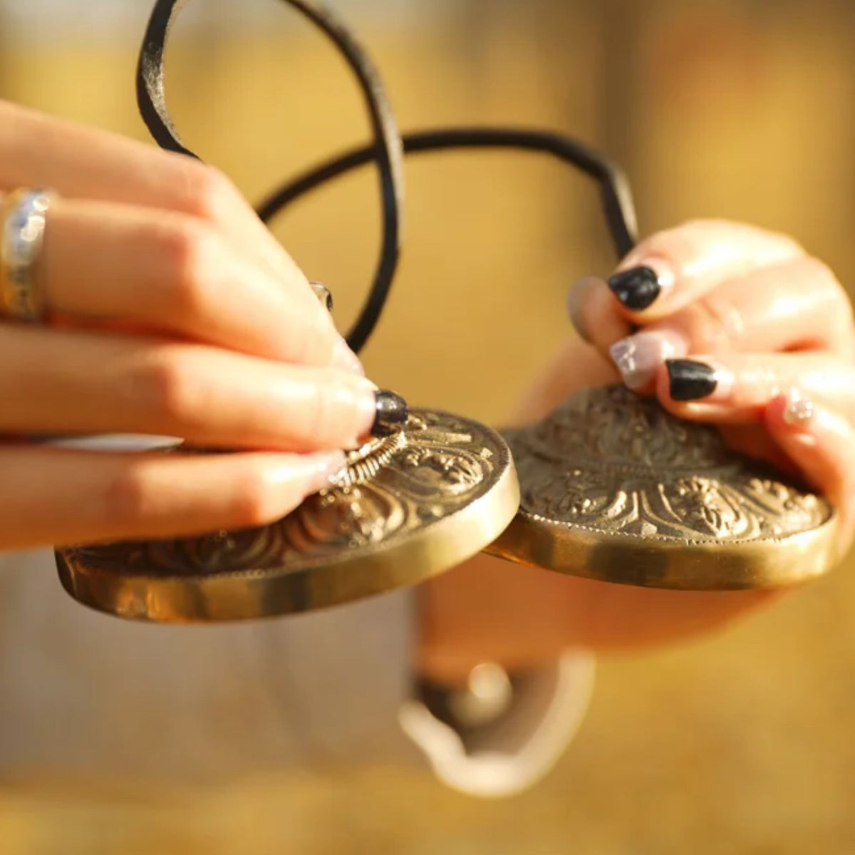 Close-up of a woman’s hands holding Meinl Sonic Energy TINGSHA-OR tingshas, showing the ornamental design.