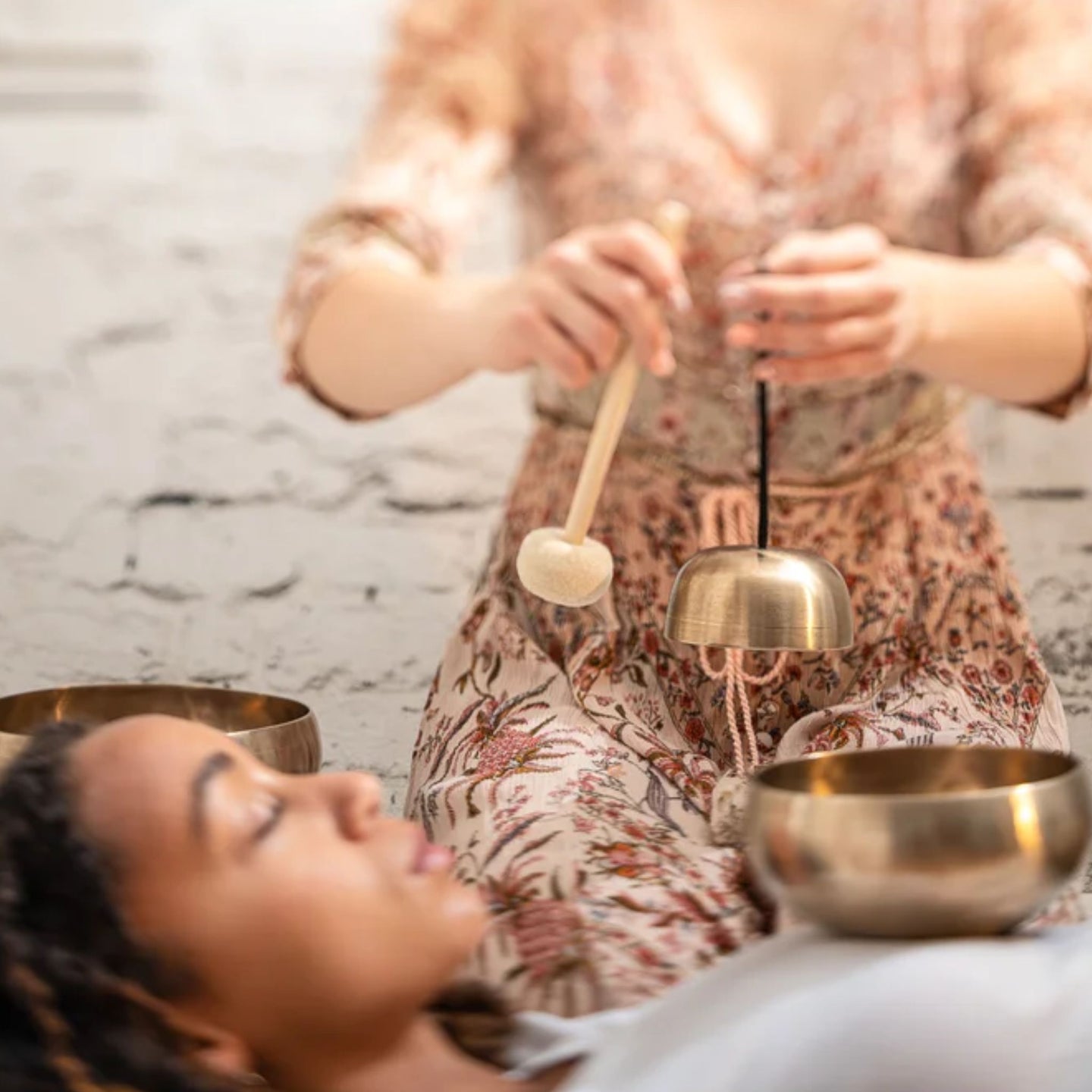 woman holding a Meinl Sonic Energy Universal Series Singing Bowl above another woman during a sound therapy session, creating resonant bronze singing bowl tones for relaxation, meditation, mindfulness, and wellness practices.