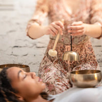 woman holding a Meinl Sonic Energy Universal Series Singing Bowl above another woman during a sound therapy session, creating resonant bronze singing bowl tones for relaxation, meditation, mindfulness, and wellness practices.