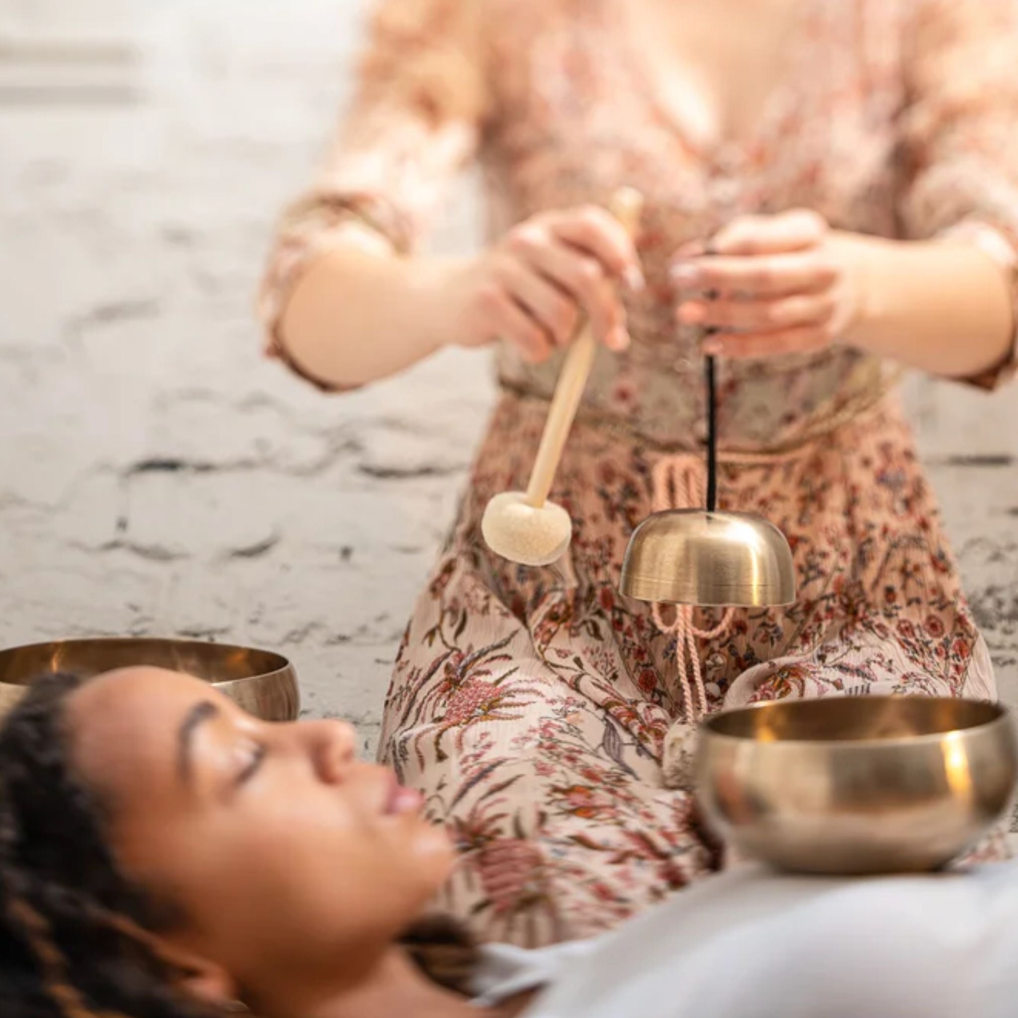 woman holding a Meinl Sonic Energy Universal Series Singing Bowl above another woman during a sound therapy session, creating resonant bronze singing bowl tones for relaxation, meditation, mindfulness, and wellness practices.