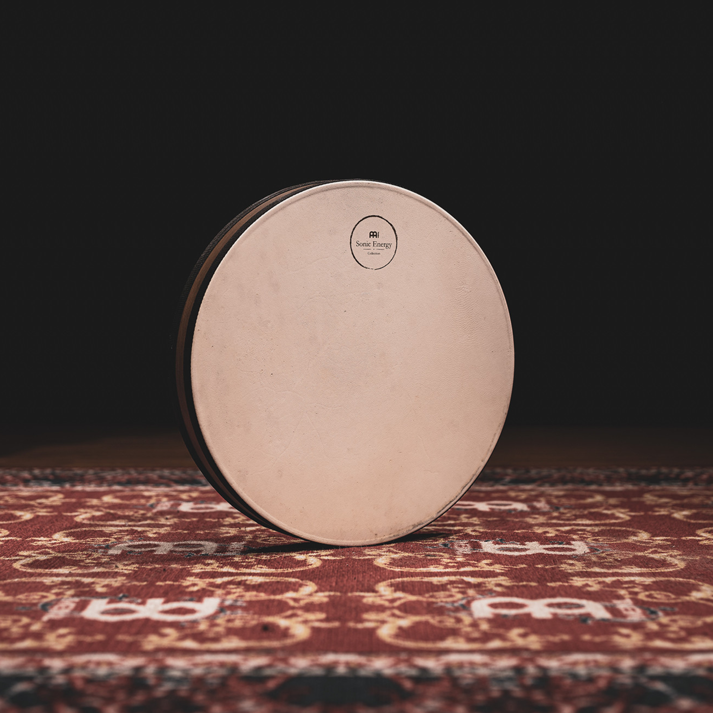 Front view of the Meinl Sonic Energy Wave Drum 16-inch in Walnut Brown featuring the natural goat-skin head resting on a rustic mat.