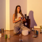 woman meditating in a candlelit room with a Meinl Sonic Energy white frosted crystal singing bowl and mallet placed in front of her, creating a peaceful setting for mindfulness, meditation, relaxation, and sound therapy practices.