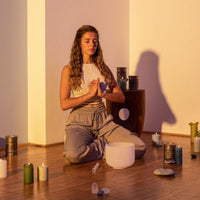 woman meditating in a candlelit room with a Meinl Sonic Energy white frosted crystal singing bowl and mallet placed in front of her, creating a peaceful setting for mindfulness, meditation, relaxation, and sound therapy practices.