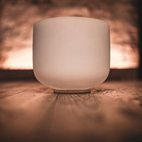 Meinl Sonic Energy white frosted crystal singing bowl displayed on a wooden surface with warm ambient lighting, showcasing the frosted quartz finish and minimalist design used for meditation, sound therapy, and immersive sound exploration.