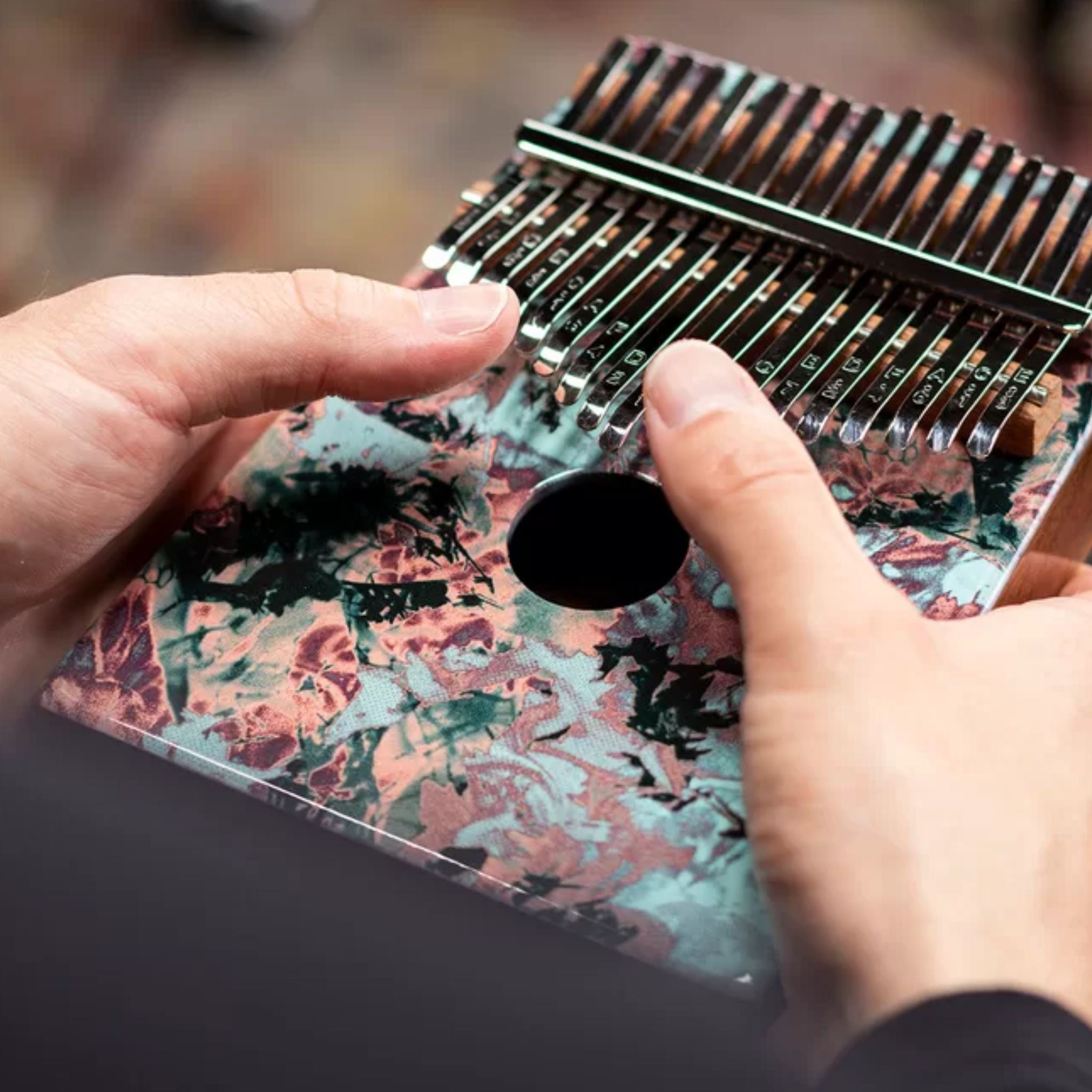person playing Meinl Sound Hole Designer Kalimba Coral Reef KA17CR showing the full top view of the 17-note kalimba with coral reef artwork, engraved tines, and acacia wood body.