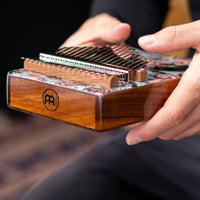 person playing Meinl Sound Hole Designer Kalimba Coral Reef KA17CR with the Meinl logo visible, showing the 17-note layout, coral reef artwork, and acacia wood body during melodic sound exploration.