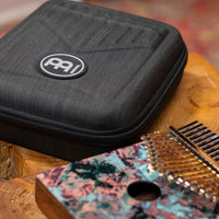 Meinl Sound Hole Designer Kalimba Coral Reef KA17CR displayed beside its protective carrying case on a rustic wooden table, showcasing the coral reef artwork, acacia wood construction, and included storage case.