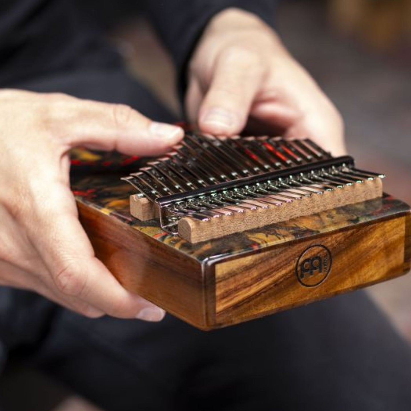 close up of hand playing Meinl Sound Hole Designer Kalimba Lava KA17LV showing engraved notes, chrome-plated steel tines, and acacia wood body producing warm melodic tones and rich resonance.