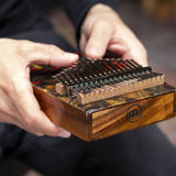 close up of hand playing Meinl Sound Hole Designer Kalimba Lava KA17LV showing engraved notes, chrome-plated steel tines, and acacia wood body producing warm melodic tones and rich resonance.