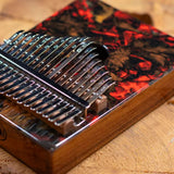 close up of Meinl Sound Hole Designer Kalimba Lava KA17LV highlighting the lava-inspired artwork, engraved note markings, chrome-plated steel tines, and acacia wood construction.