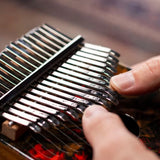extreme close up of two thumbs playing the Meinl Sound Hole Designer Kalimba Lava KA17LV showing engraved steel tines and precise finger technique used to create melodic and resonant kalimba tones.